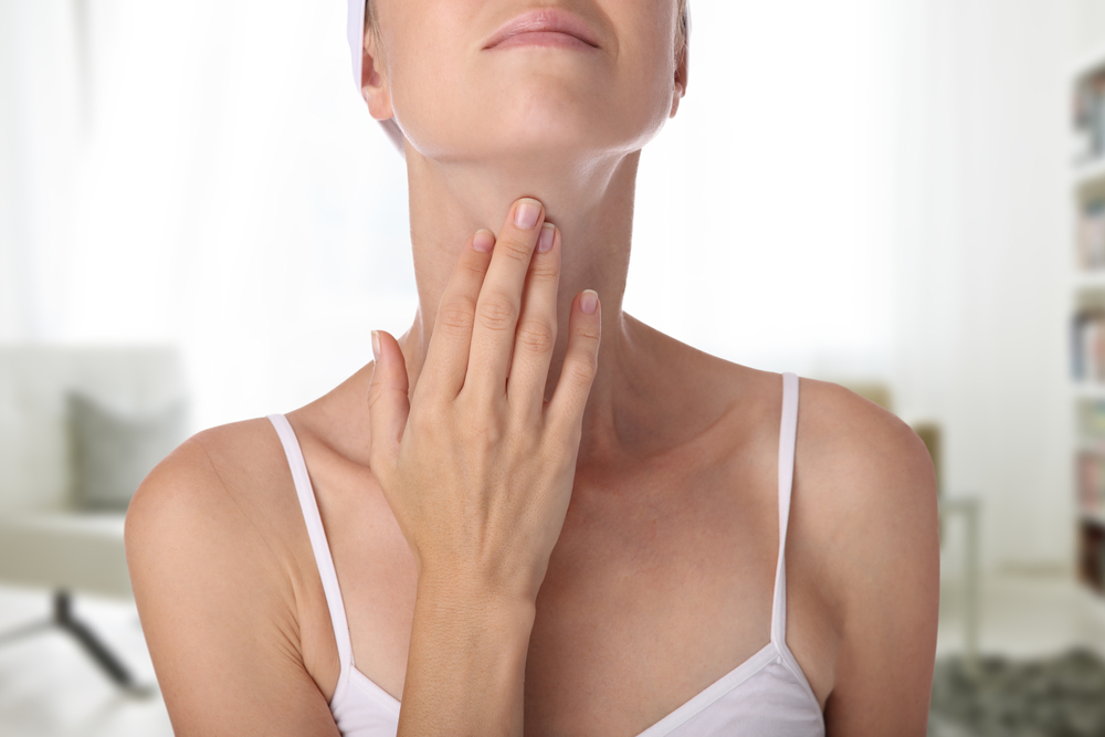 Woman holding hand up to her throat where the thyroid is located