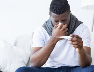 Sick african american guy covered with scarf holding thermometer, having fever, empty space