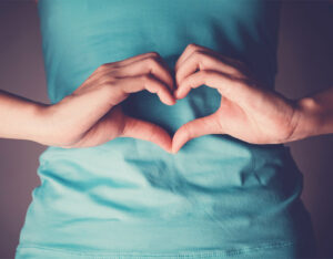 woman with heart hands over her gut, indicating gut health