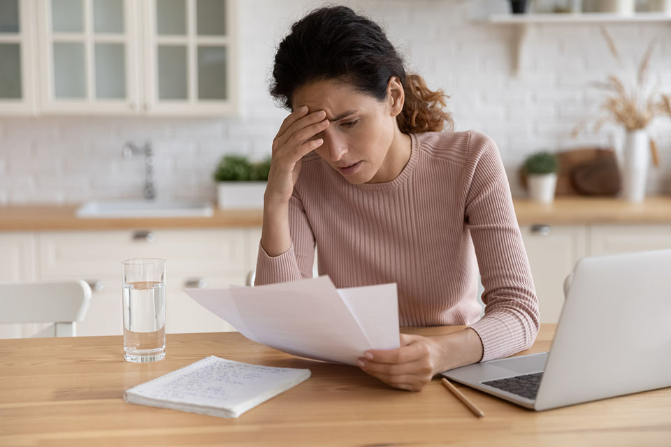 Woman at home reviewing paperwork, thoughtful expression